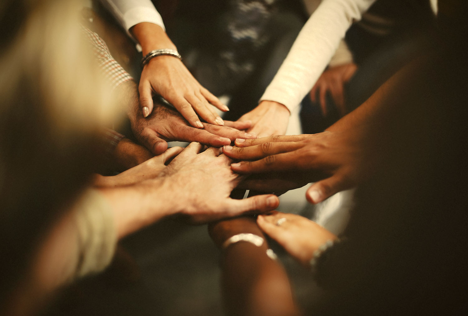 A group of hands all placed on top of one another. The hands have different skin tones.